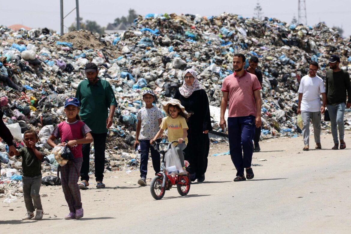 Gazans walking past rubbish piles in Khan Younis