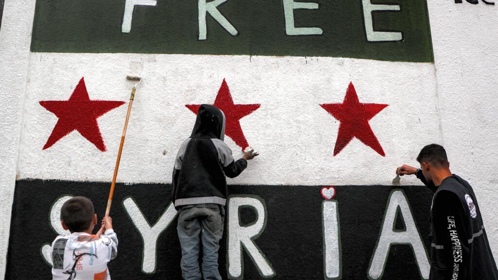 A man and children paint a mural of the Syrian flag in Homs